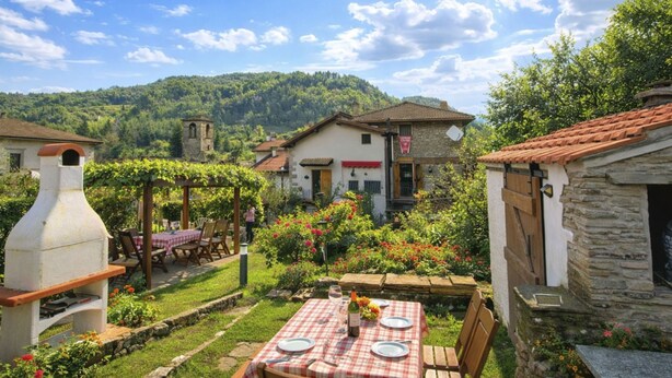 A rustic outdoor dining area with a checkered tablecloth, a stone oven, and a stone building in the background. - Apartment Torre by Interhome (Palazzuolo Sul Senio)
