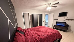 Une chambre à coucher avec un lit, un ventilateur de plafond, une télévision et une armoire.