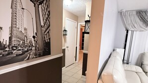 Un couloir orné d’une fresque représentant un paysage urbain, un canapé blanc et une porte donnant sur une autre pièce.