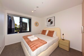 A bedroom with a large bed, a bedside table, a window, and a wall-mounted artwork. - Stylish Manchester Street City Stay (Christchurch)