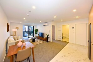 A modern living room with a sofa, dining table, TV, and a balcony view. - Stylish Manchester Street City Stay (Christchurch)