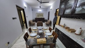 A dining area with a glass table, chairs, and a kitchen with cabinets and a countertop. - Modern 2BR in Elite DOHS Baridhara – Secure, Quiet & Stylish (Dhaka)