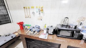 A kitchen with a gas stove, microwave, kettle, and various utensils on the counter. - Modern 2BR in Elite DOHS Baridhara – Secure, Quiet & Stylish (Dhaka)