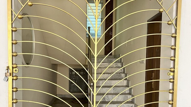 A golden metal gate with a leaf-like design, leading to a staircase with marble steps. - Modern 2BR in Elite DOHS Baridhara – Secure, Quiet & Stylish (Dhaka)