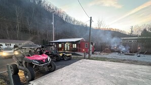 A rural setting with ATVs parked in front of a red building, a wooden fence, and a clear sky. - Peaceful 2-bedroom cabin with AC in charming Delbarton (Delbarton)