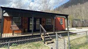A small, single-story building with a porch, a wooden bench, and a small table. - Peaceful 2-bedroom cabin with AC in charming Delbarton (Delbarton)