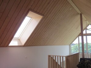 Una habitación con techo de madera inclinado, tragaluz y vista a la vegetación exterior.