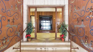 A grand staircase leading to a room with a large window, flanked by ornate wall decorations and potted plants.
