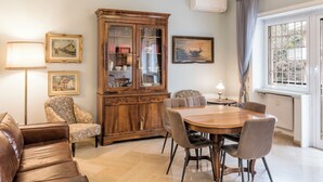 A dining area with a wooden table and chairs, a cabinet with glass doors, and a window with curtains.