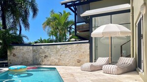 A swimming pool with lounge chairs, a stone wall, and a glass door leading to a balcony. - Tranquility on Buderim - large, light family home with expansive views. (Buderim)