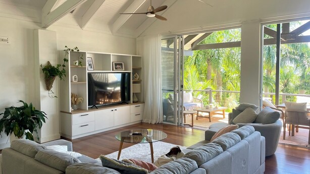 A spacious living room with a large flat-screen TV, a sofa, a coffee table, and a balcony with outdoor furniture. - Tranquility on Buderim - large, light family home with expansive views. (Buderim)