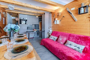 Una cucina compatta con elettrodomestici moderni, un'area pranzo con tavolo in legno apparecchiato per quattro persone e un comodo divano rosso.