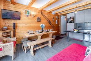 Ein Holzinnenraum mit einem für vier Personen gedeckten Esstisch, einer Küchenzeile und einem an der Wand montierten Fernseher.