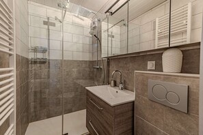 Ein modernes Badezimmer mit einer gläsernen Duschkabine, einem Waschtisch und einem Handtuchhalter.