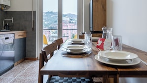 Un comedor con una mesa dispuesta para cuatro, una cocina equipada con lavavajillas y vistas a un paisaje urbano a través de un ventanal grande.