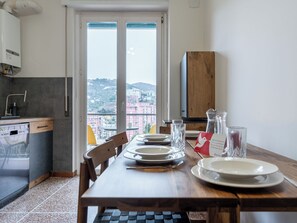 Ein Essbereich mit Tisch für vier Personen, eine Küche mit Geschirrspüler und Blick auf eine Stadtlandschaft durch ein großes Fenster.