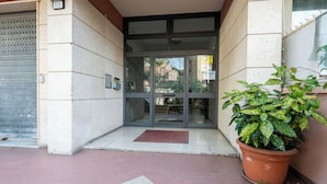 Entrada de un edificio con puerta de vidrio, una planta en maceta y un detector de incendios en la pared.