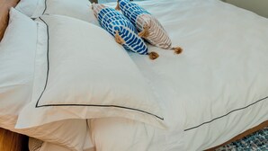 A bed with white bedding and two decorative pillows, a wooden headboard, and a window with a view. - Cozy Modern Stayz | Free Parking | 1-Min Station, 5-Min Hospital | Heated Pool (Wollongong)