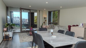 A modern apartment with a dining area, kitchen, and a balcony with a city view. - Cozy Modern Stayz | Free Parking | 1-Min Station, 5-Min Hospital | Heated Pool (Wollongong)