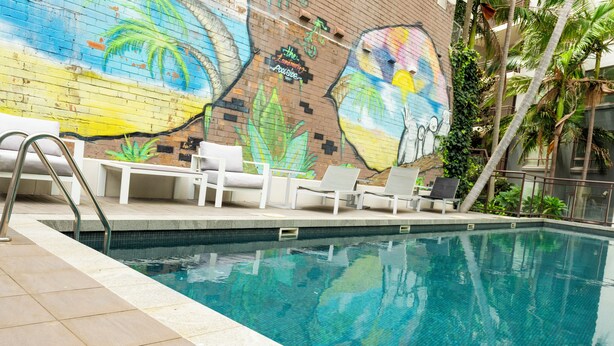 A swimming pool with a mural, white lounge chairs, and a tiled deck. - Cozy Modern Stayz | Free Parking | 1-Min Station, 5-Min Hospital | Heated Pool (Wollongong)