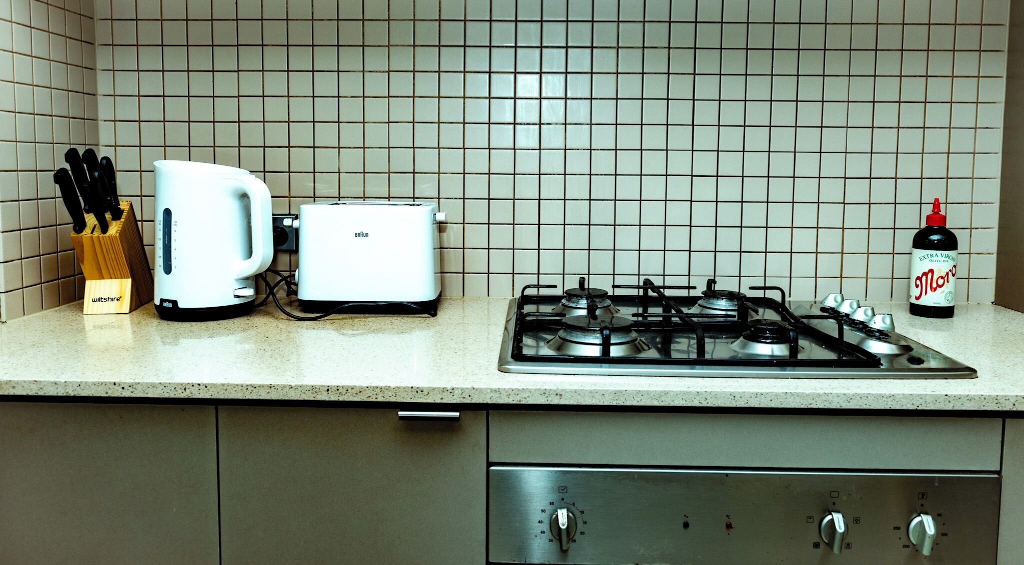 Una cocina con estufa a gas, un tostador y una botella de aceite de oliva.