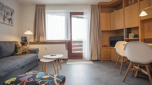 Een moderne woonkamer met een bank, een klein tafeltje, een stoel, een televisie en een keukenhoek.