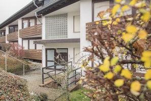 Ein Mehrfamilienhaus mit Balkonen, einem überdachten Eingangsbereich und einem kleinen Garten.