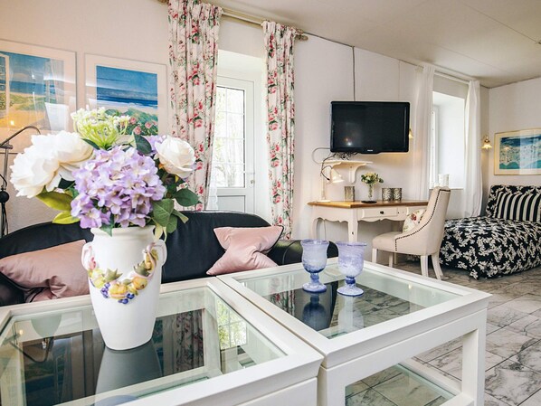 A living room with a glass coffee table, a sofa, a chair, a television, and a floral vase.
