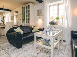 A living room with a black leather sofa, a white coffee table, and a glass-top table with blue glassware.