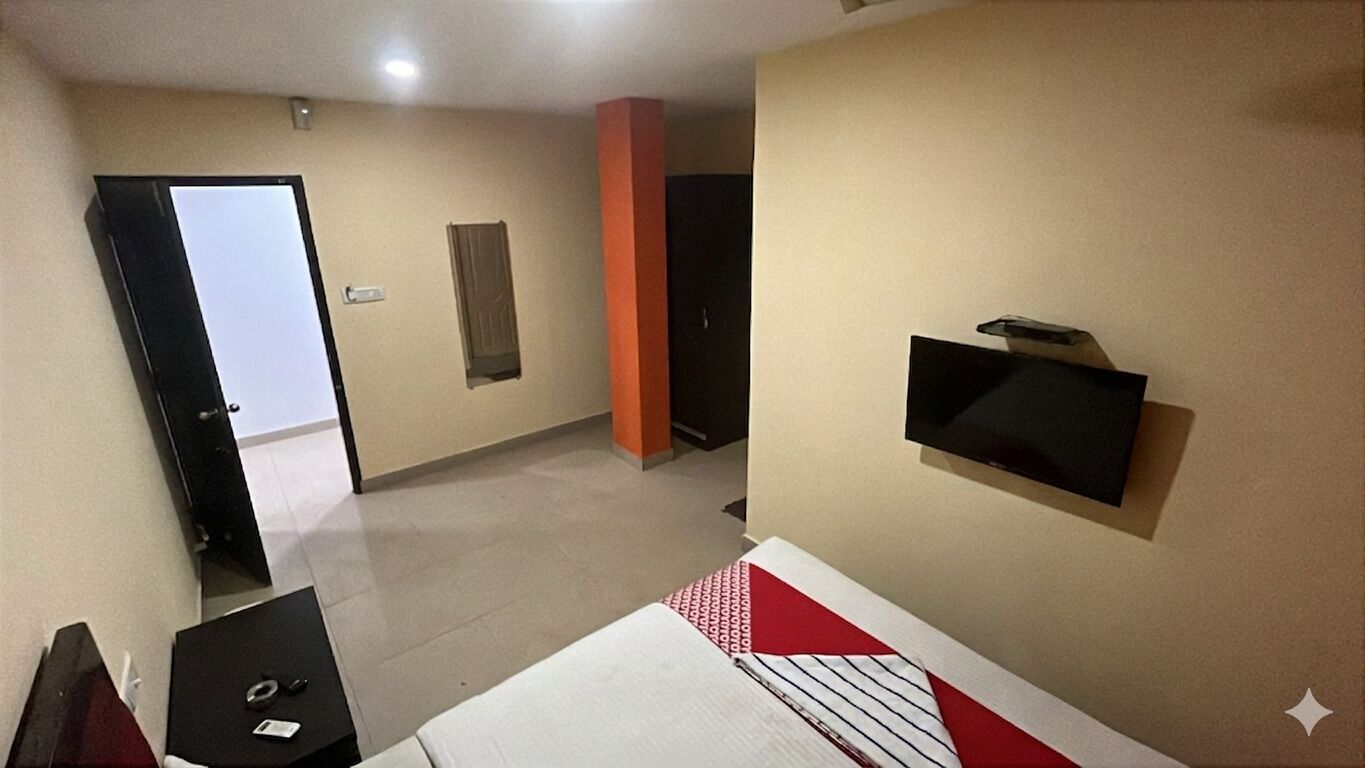 A hotel room with a bed, a TV mounted on the wall, a desk with a chair, and a door leading to another room.