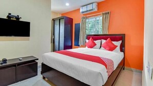 A hotel room with a bed, a desk, a TV, and an air conditioning unit.
