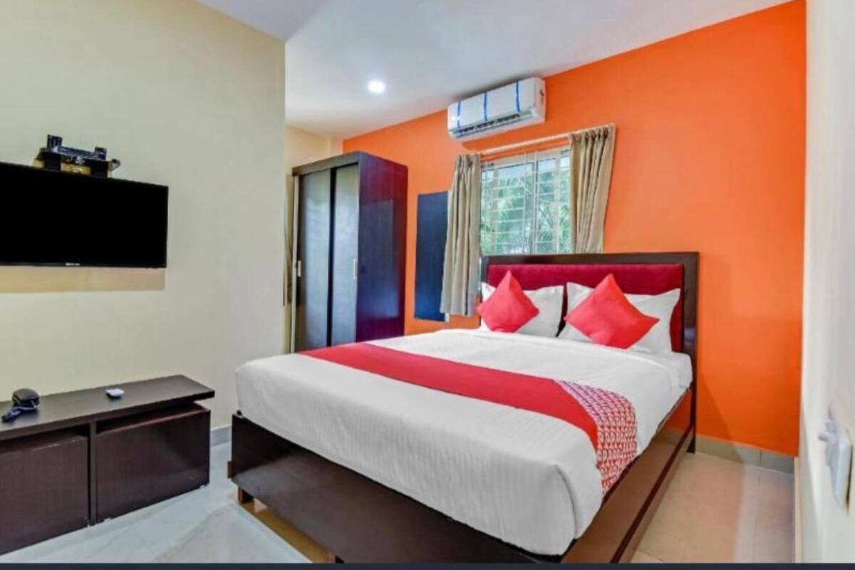 A hotel room with a bed, a desk, a TV, and an air conditioning unit.