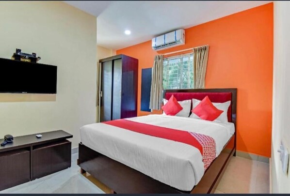 Una habitación de hotel con cama, escritorio, televisor y aire acondicionado.