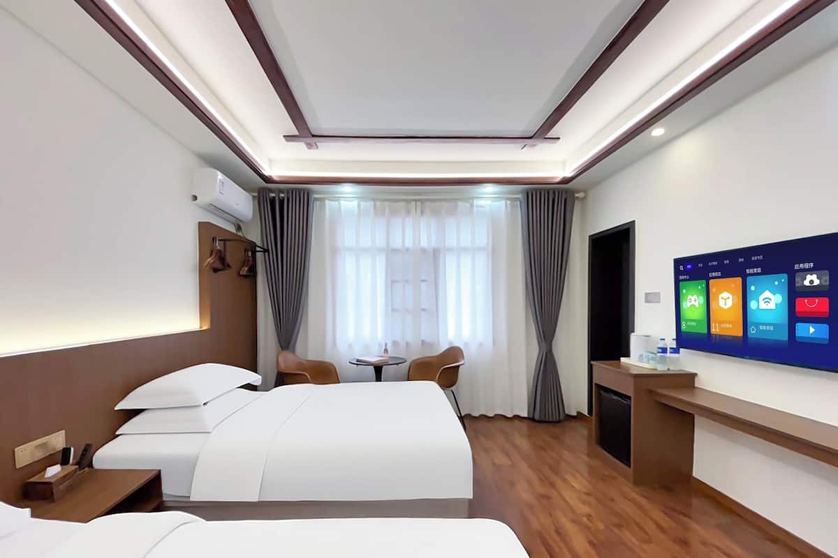 A hotel room with two beds, a desk, a TV, and a window with curtains.