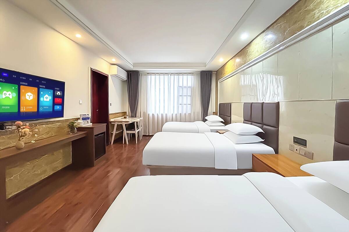 A hotel room with a TV, a desk, two beds, and a window with curtains.