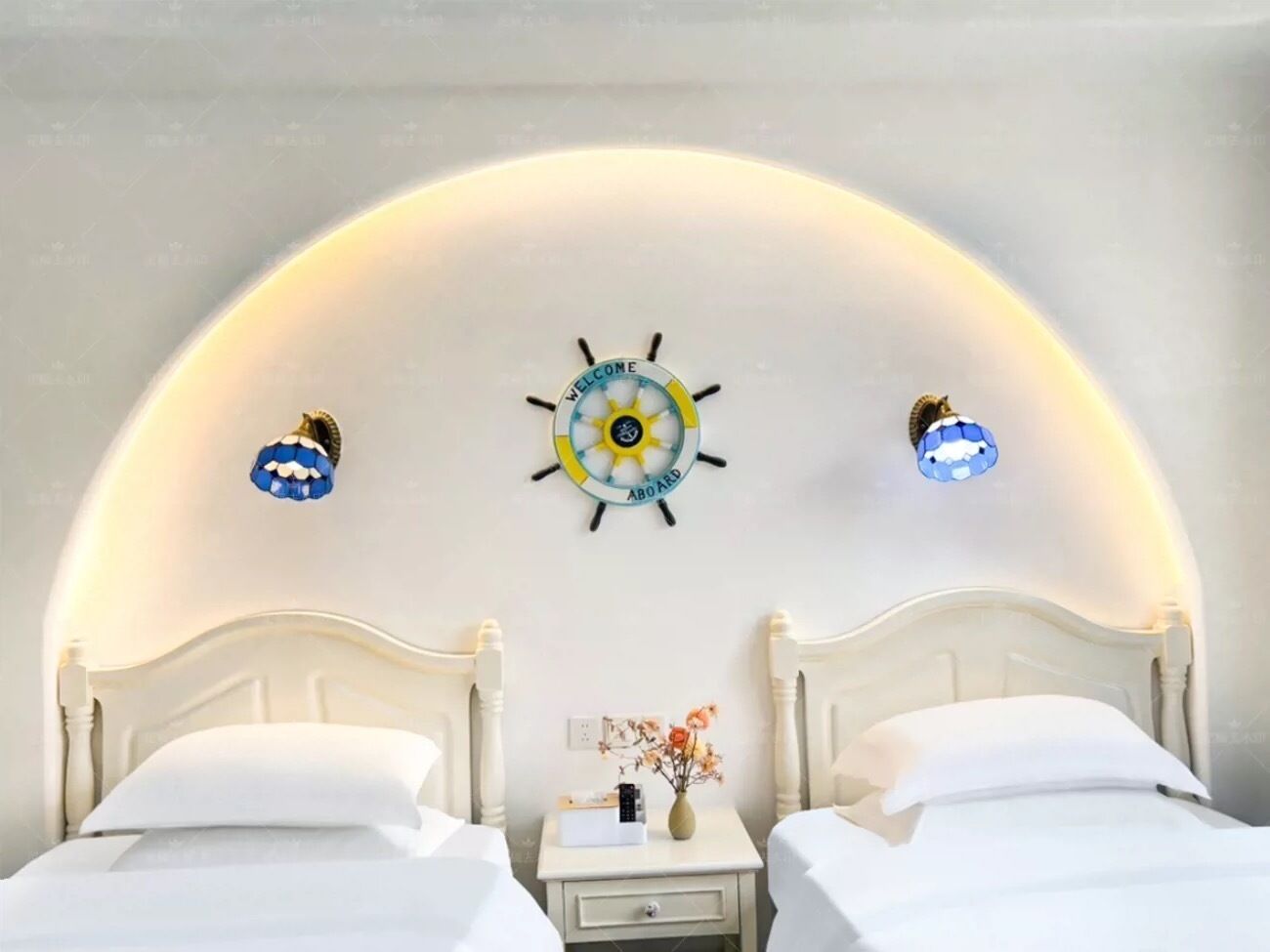 A hotel room with two white beds, a small bedside table with a vase of flowers, and a wall-mounted decorative piece.