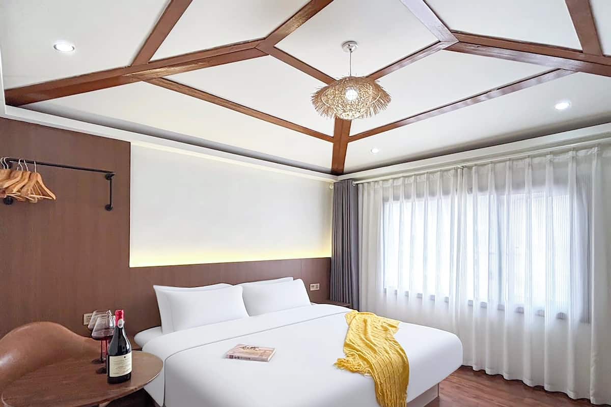 A hotel room with a large bed, a wooden ceiling, a chandelier, a dining table with wine, and a view of the outdoors.