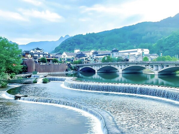 A river with multiple waterfalls, a bridge, and traditional buildings in the background.