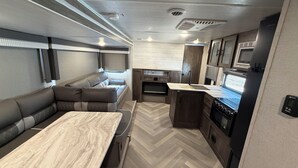 A compact RV interior with a kitchenette, a dining area, and a seating area. - Family Friendly Bunkhouse RV (Jasper)
