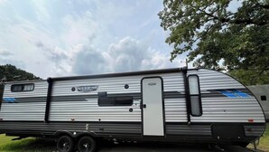 A large RV with a sliding door, a small window, and a side panel with a logo. - Family Friendly Bunkhouse RV (Jasper)