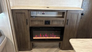 A fireplace with a control panel, a power outlet, and a thermostat. - Family Friendly Bunkhouse RV (Jasper)