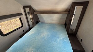 A compact RV interior with a blue floor, wooden walls, and two windows. - Family Friendly Bunkhouse RV (Jasper)