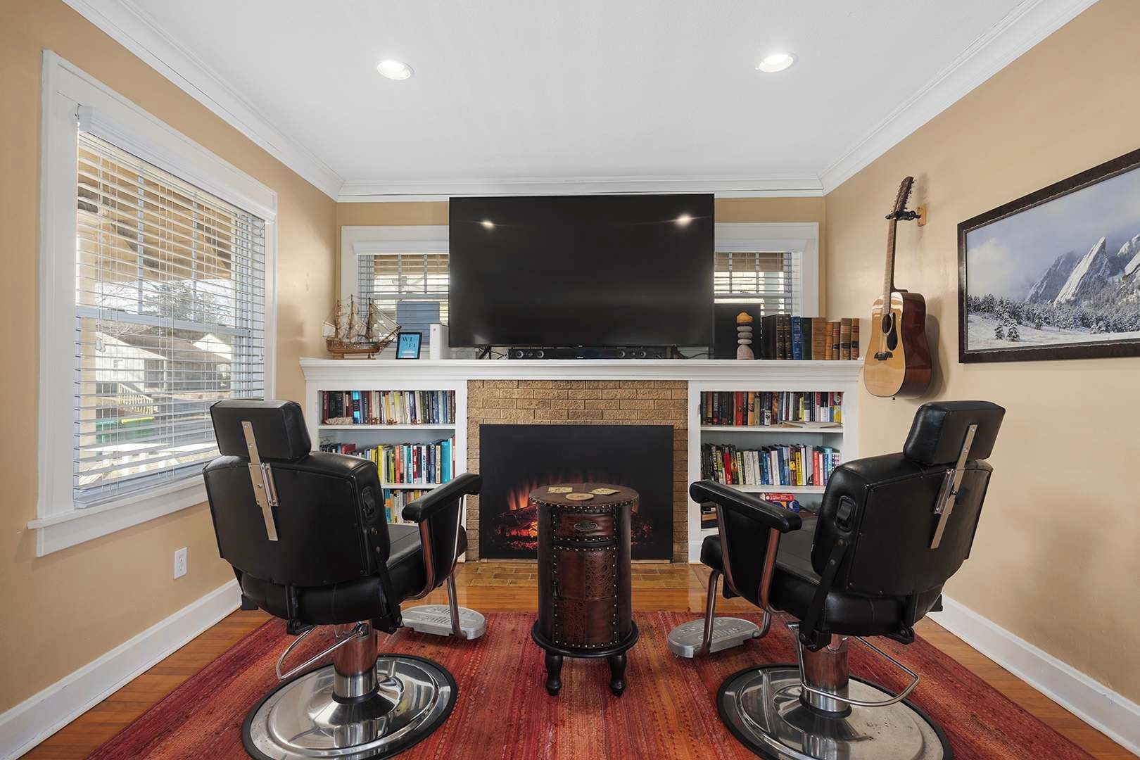 A living room with a fireplace, a large flat-screen TV, and two leather chairs.
