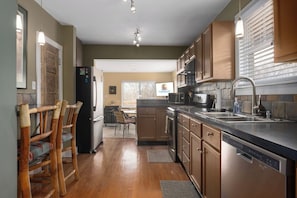 A kitchen with wooden cabinets, a stainless steel dishwasher, and a built-in oven. - Cozy Stay_30 Days or More_Fenced Yard_Workspace (Kansas City)