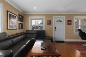 A living room with a black leather sofa, a wooden coffee table, and a door with a glass panel. - Comfortable Cozy Home,30 Day Stays_Sleeps8 (Kansas City)