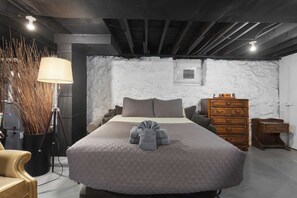 A bedroom with a large bed, a wooden dresser, a lamp, and a wall-mounted heater. - Cozy Stay_30 Days or More_Fenced Yard_Workspace (Kansas City)