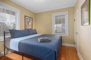 A bedroom with a bed, two windows with blinds, a door, and a framed picture on the wall. - Comfortable Cozy Home,30 Day Stays_Sleeps8 (Kansas City)