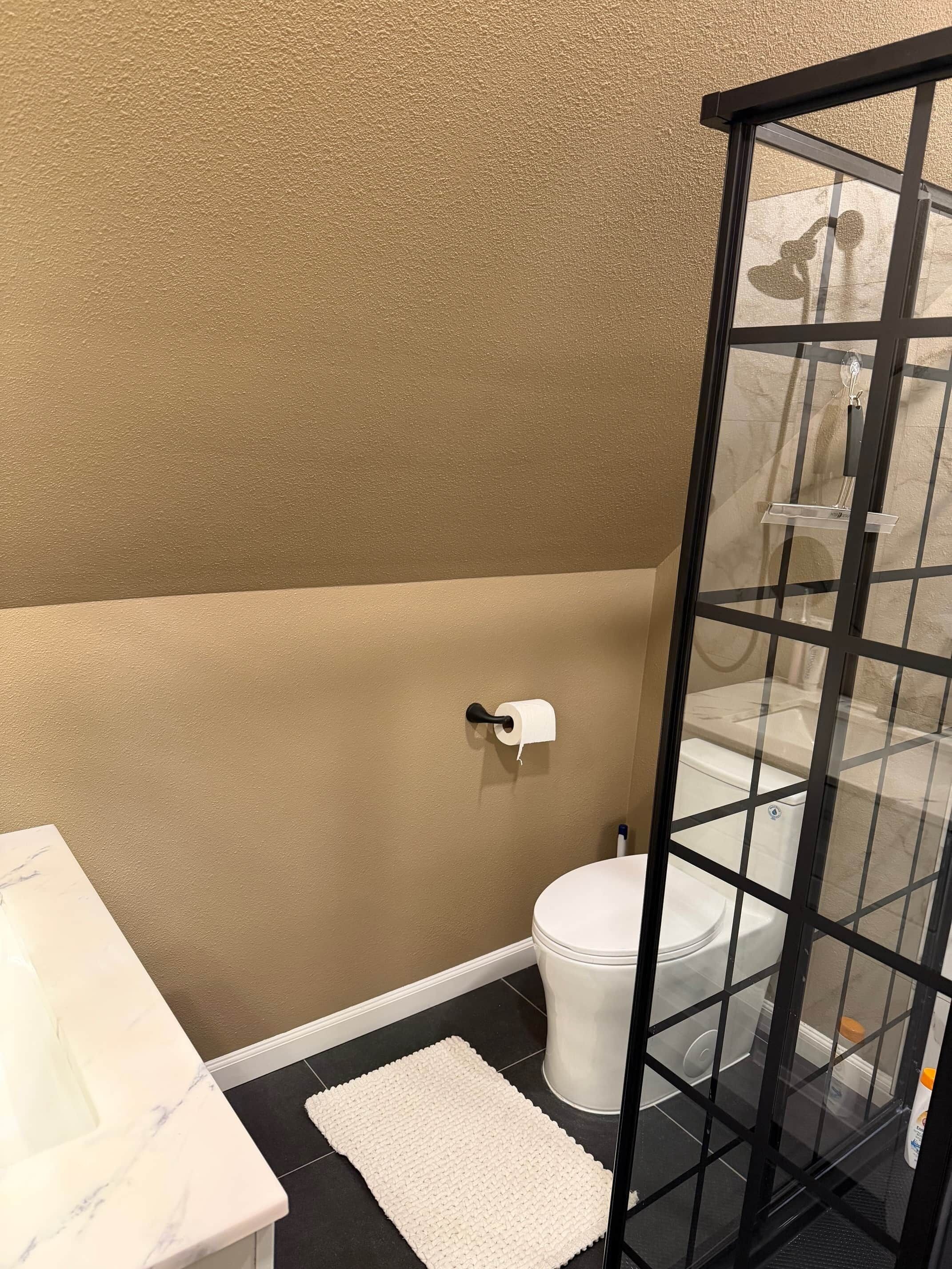 A bathroom with a toilet, a glass shower enclosure, a white sink, and a beige wall.