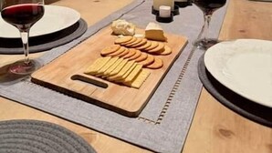 Une table de salle à manger en bois, avec une planche à fromage, des verres à vin et des bougies.