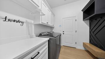 A modern kitchen with white cabinetry, a stainless steel washer, a built-in oven, and a black accent wall.